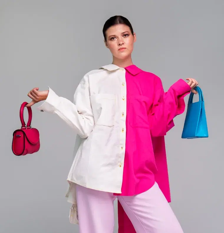 A woman in a half white, half pink shirt holding a red bag and a blue bag